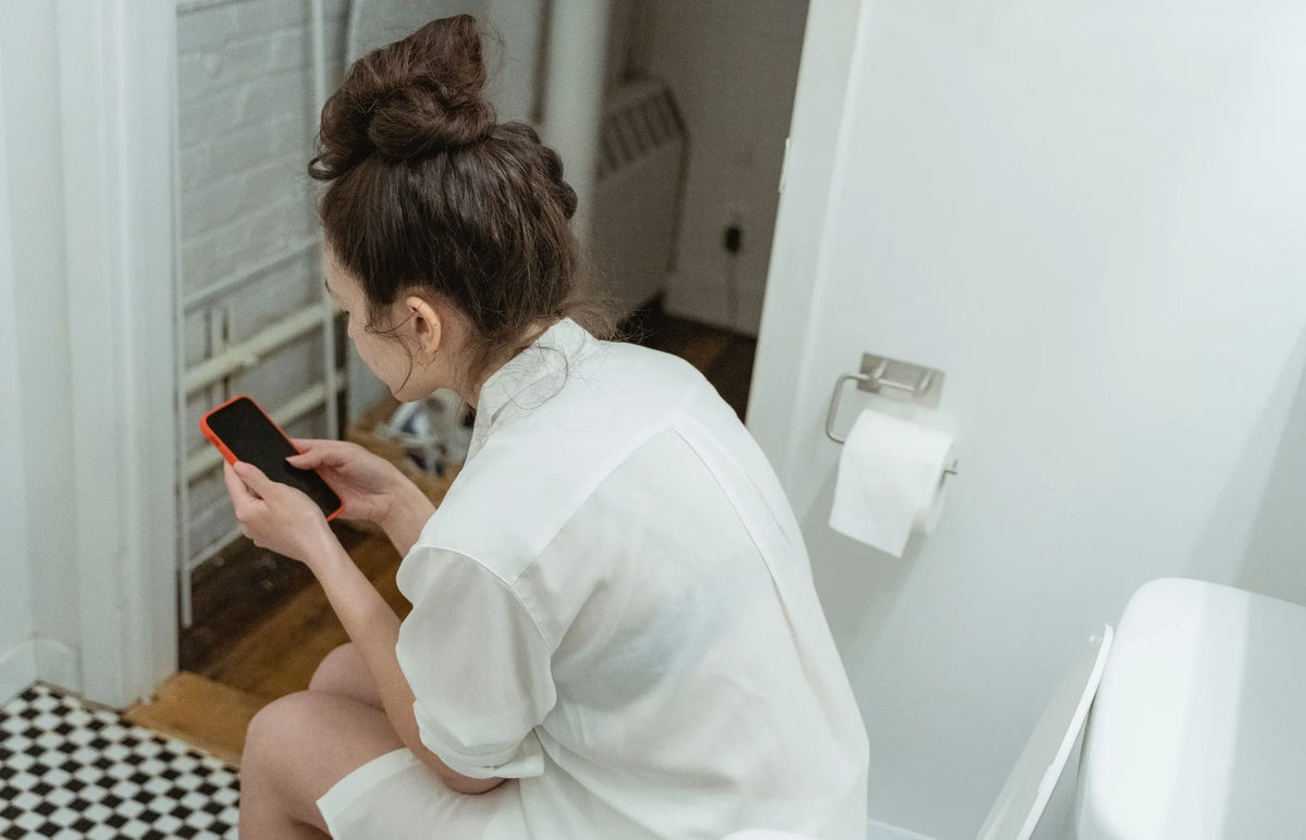 woman in a white robe scrolling on the toilet