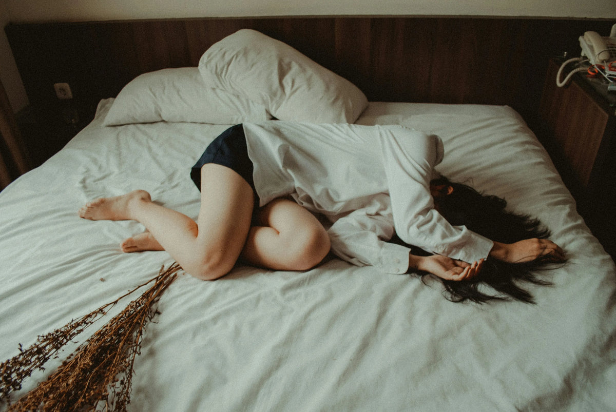 woman laying in bed, seemingly feeling unwell