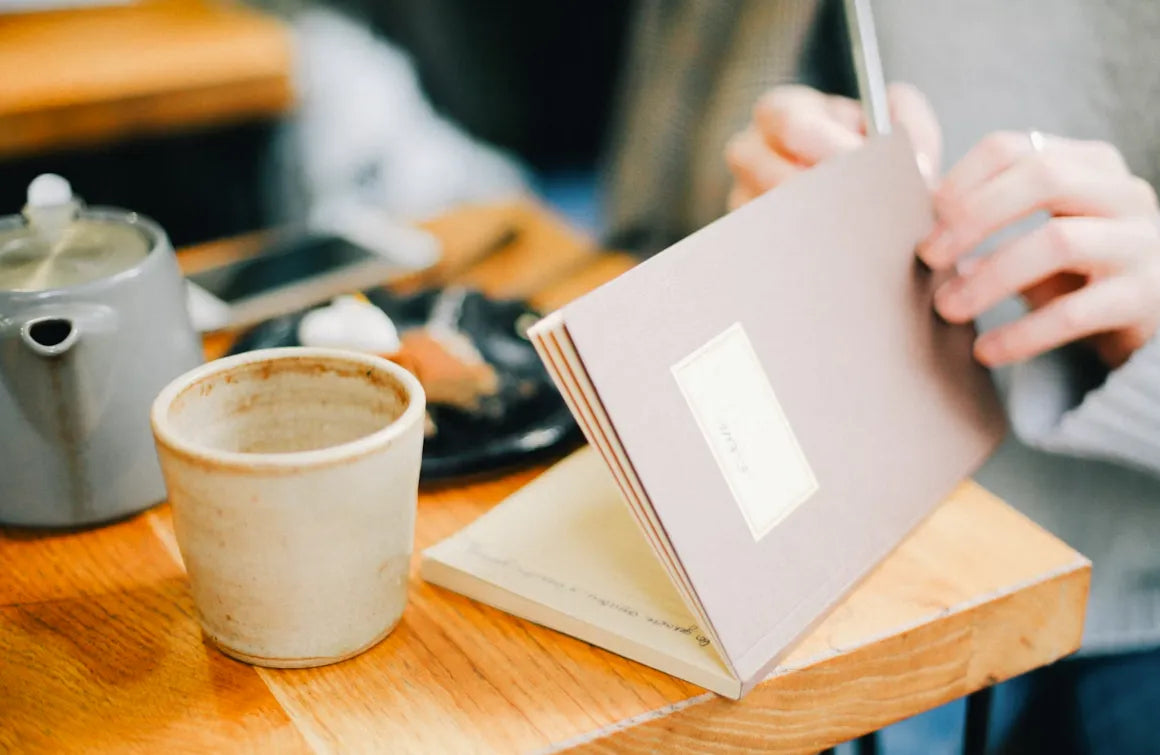 Person writing notes beside a cup of coffee
