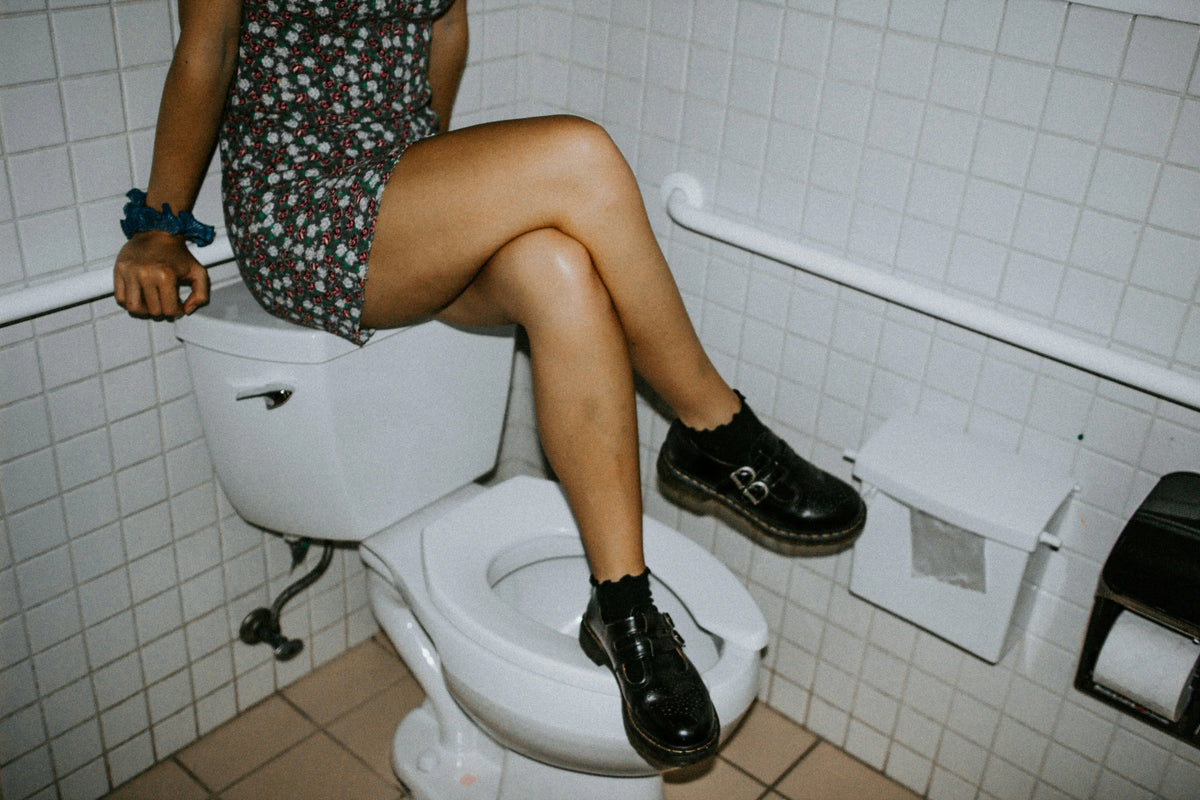 woman in boots sitting on top of a toilet