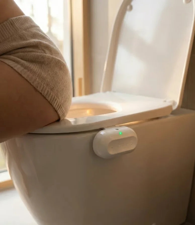 Someone resting on the edge of a toilet with the Throne sensor clipped on, in warm light